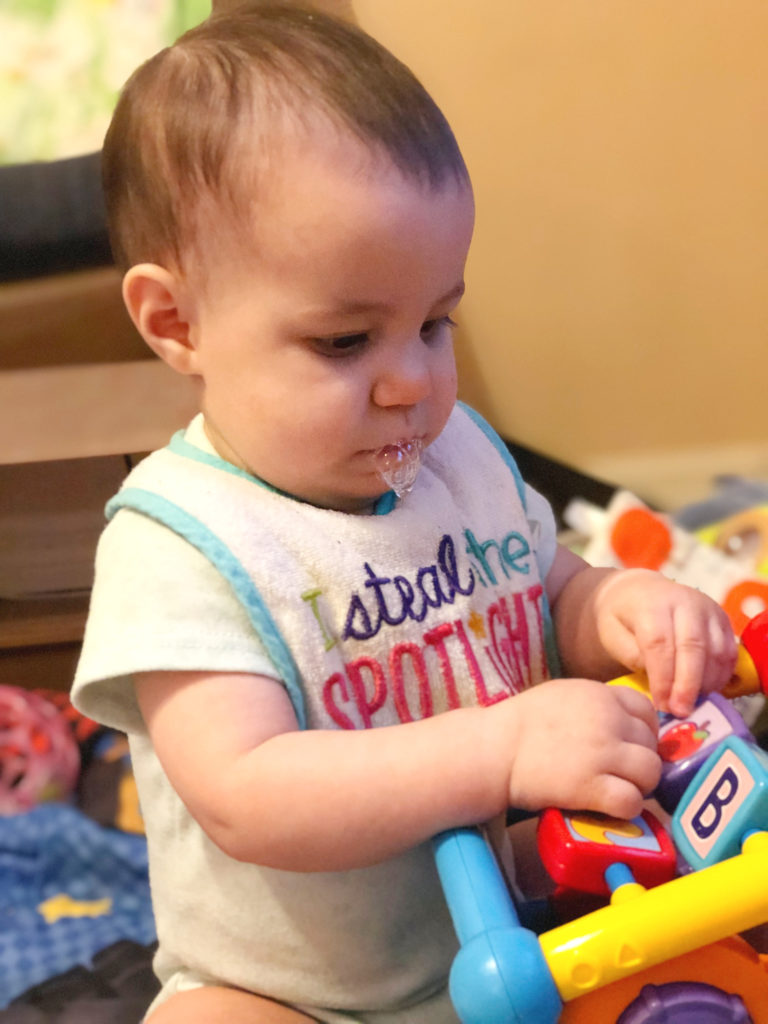 A cleft palate baby playing with a toy while wearing a cloth bib, with drool bubbles on her chin.