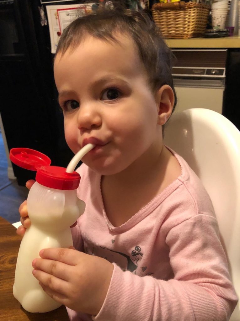 A toddler drinking milk from a straw cup shaped like a honey bear
