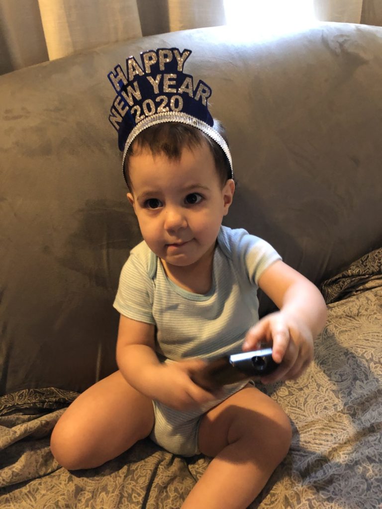 A toddler girl holding a remote control and wearing a "Happy New Year 2020" headband