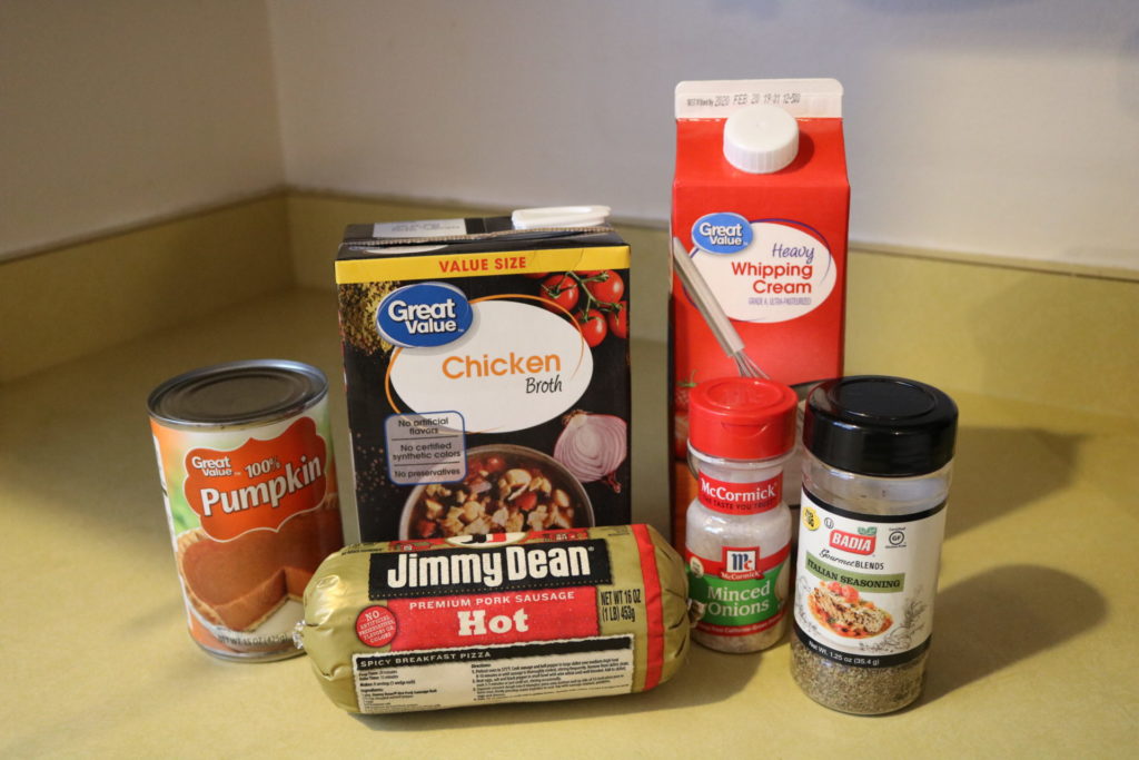 A can of pumpkin, a carton of heavy cream, a carton of chicken broth, Jimmy Dean hot sausage, minced onions, and Italian seasoning on a kitchen countertop