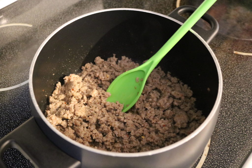 Browned sausage in a black pot with a green spoon