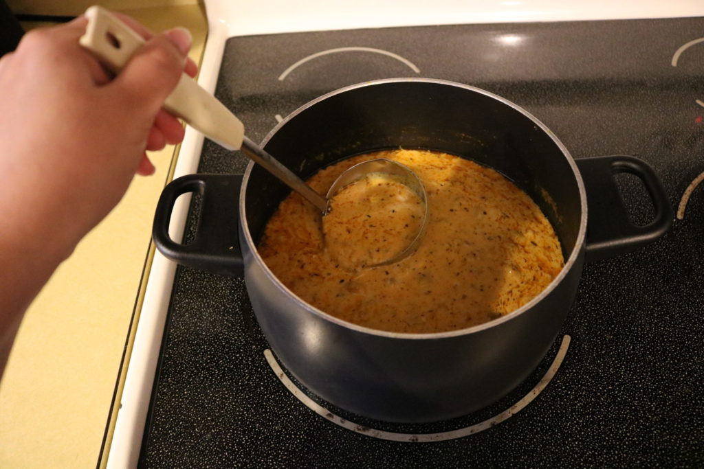 A hand ladling soup out of a black pot