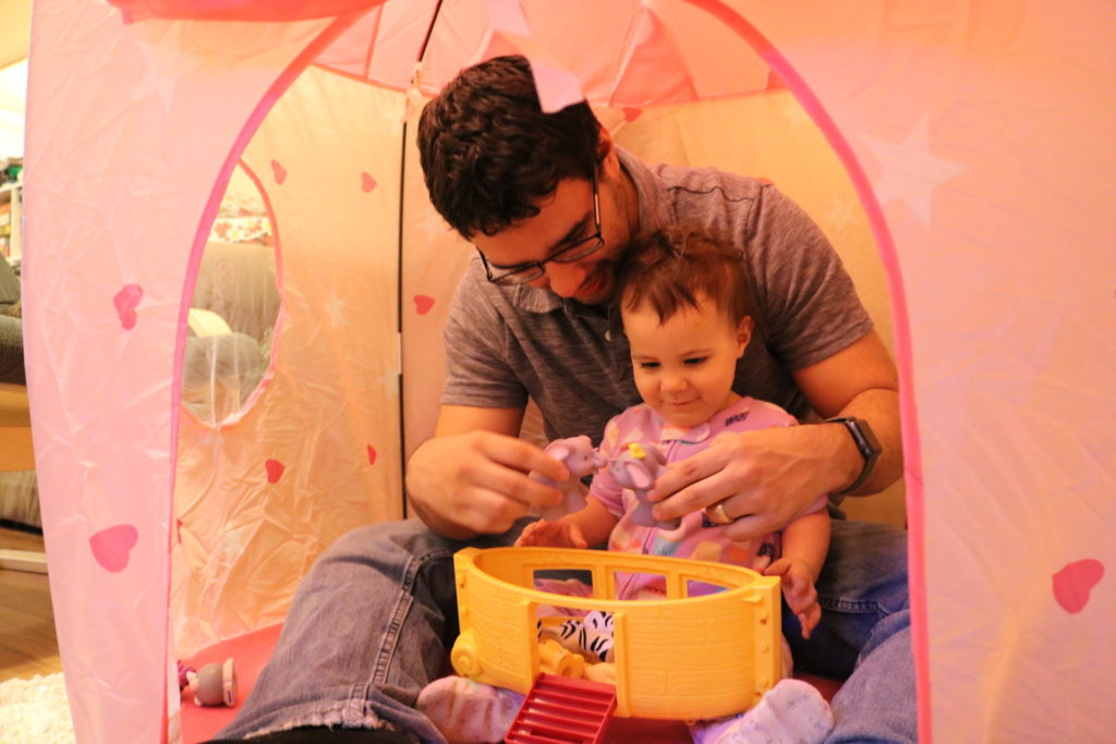 A toddler girl and a man sitting in a pink tent playing with toy animals