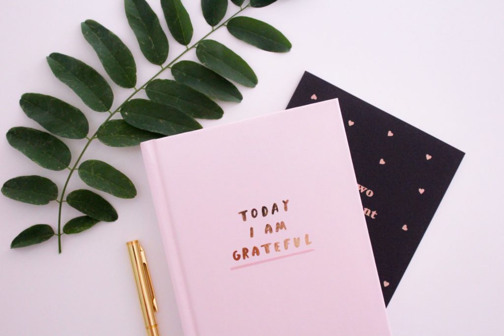 A journal with the words "Today I am grateful" next to a plant and a gold pen