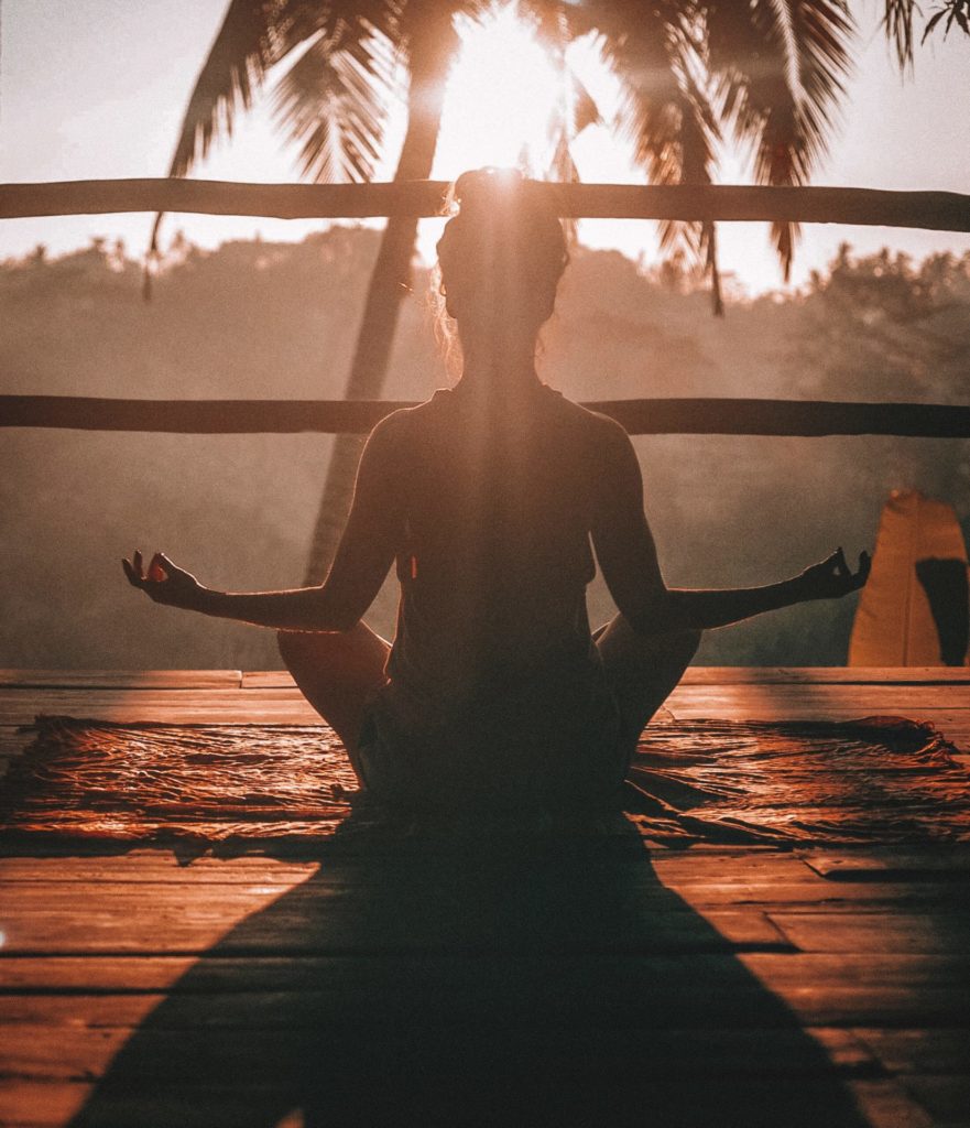 The silhouette of a woman meditating outdoors in the sunlight