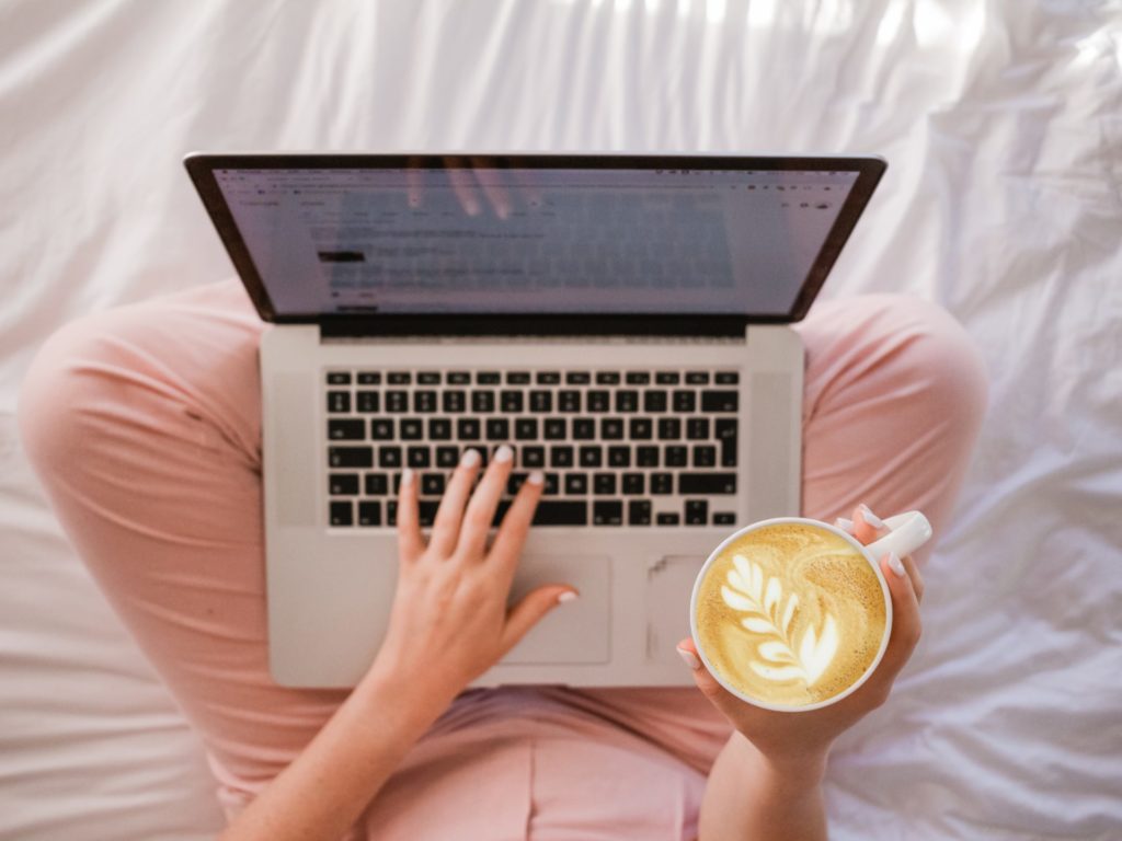 A woman sitting with a laptop in her lap and holding a cappucino