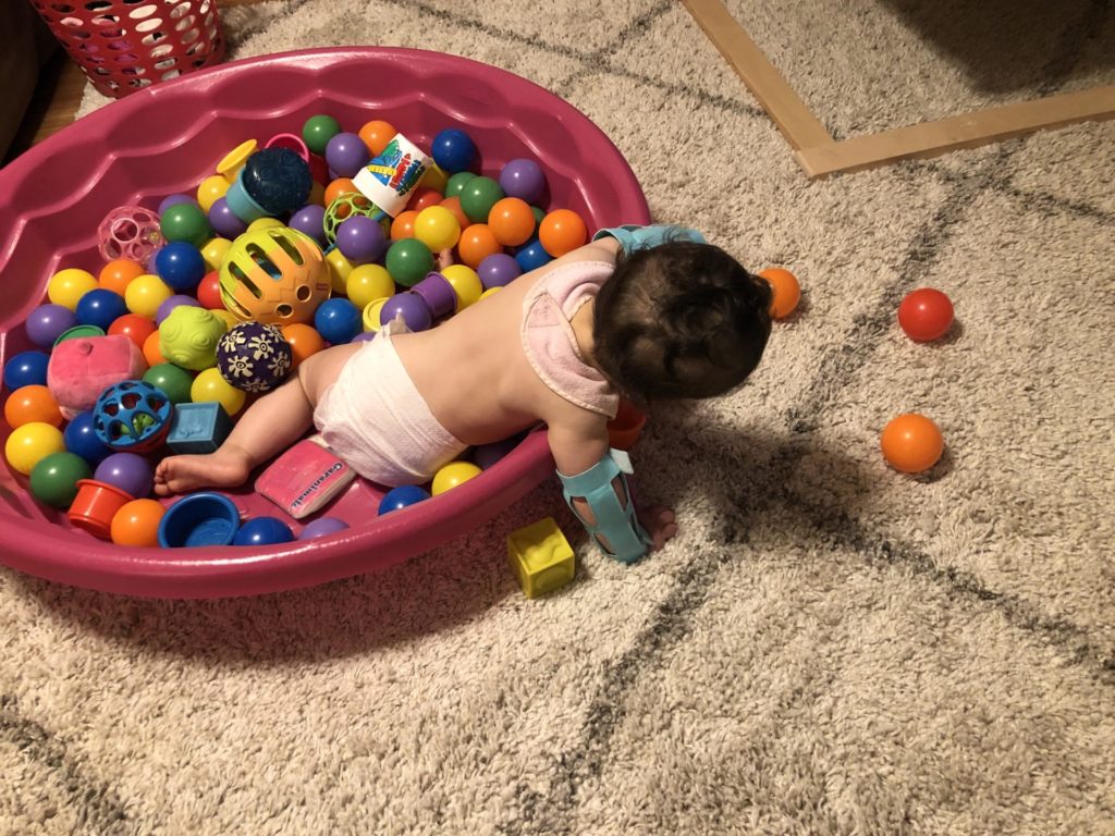 A baby playing with balls while wearing arm restraints after palate repair surgery