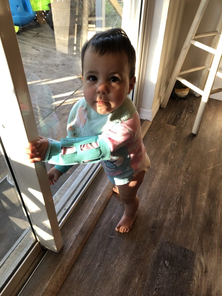 A baby wearing a long sleeved pink onesie under arm restraints after palate repair surgery